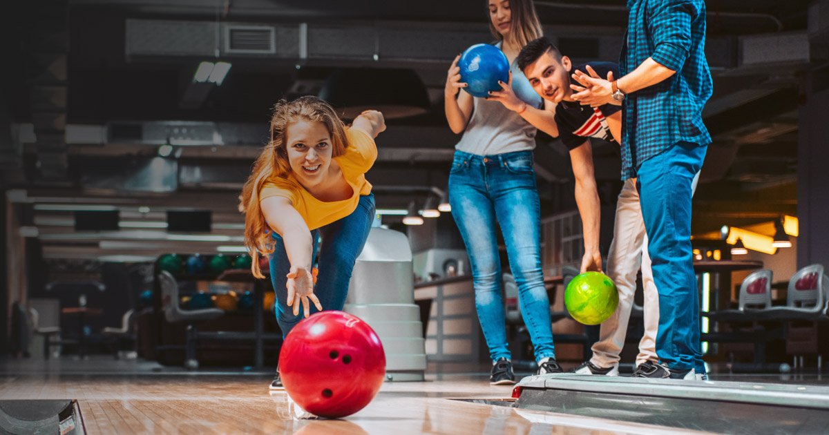 Woman bowling with her team looking on