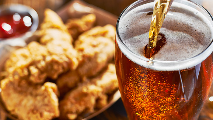 beer being poured into a glass with food in the background